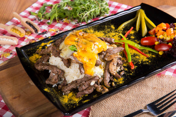istock White Rice Risotto with grilled mutton meat, boiled green pea, sliced tomato, green pickles, raw pepper and dried thyme for decoration black serving plate on brown burlap sack table cloth. 843441172