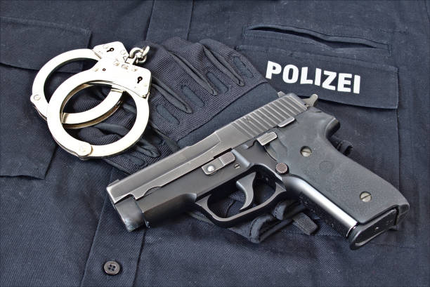 Handgun with handcuffs and gloves on blue uniform shirt with ""Police"" in German on it stock photo