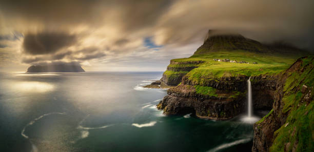 Gasadalur and Mykines Panorama of Gasadalur village and cloudy Mykines island in sunset, Faroe Islands mykines faroe islands photos stock pictures, royalty-free photos & images