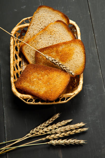 Toasts of bread and wheat on a black wooden background