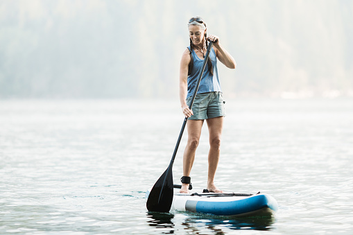 An active woman in her late 50's enjoys being out on her standup paddleboard (SUP) in the Pacific Northwest.  Shot in Washington State.