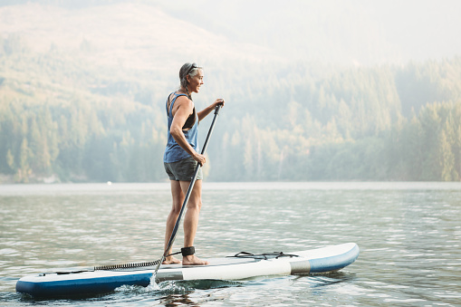 An active woman in her late 50's enjoys being out on her standup paddleboard (SUP) in the Pacific Northwest.  Shot in Washington State.