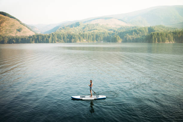 Mature Woman Paddleboarding An active woman in her late 50's enjoys being out on her standup paddleboard (SUP) in the Pacific Northwest.  Shot in Washington State. paddleboard photos stock pictures, royalty-free photos & images