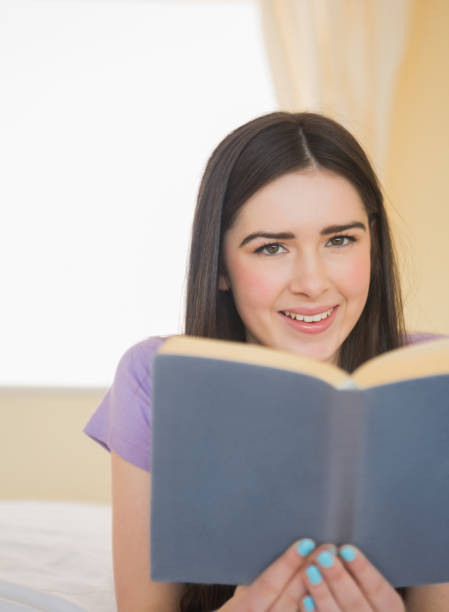 istock Happy girl looking and lying on bed reading a book 843477302