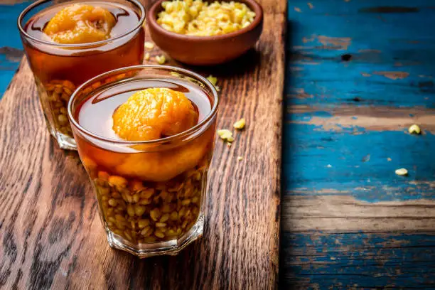 Photo of Mote con huesillo. Traditional Chilean drink made from cooked husked wheat and dried peach on wooden board, rustic blue background