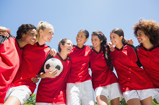 Happy female soccer team with ball against clear blue sky