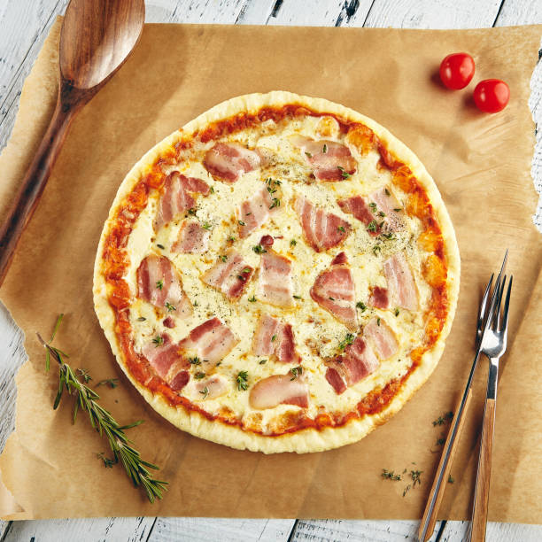 Pizza Carbonara with bacon, mozzarella cheese and creamy tomato sauce sprinkled with rosemary and lying on paper. Top View