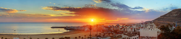 Beach in Agadir city at sunset, Morocco Panorama view of long, wide beach in Agadir city at sunset, Morocco. The hill bears the inscription in Arabic: God, Country, King sunset agadir marocco stock pictures, royalty-free photos & images