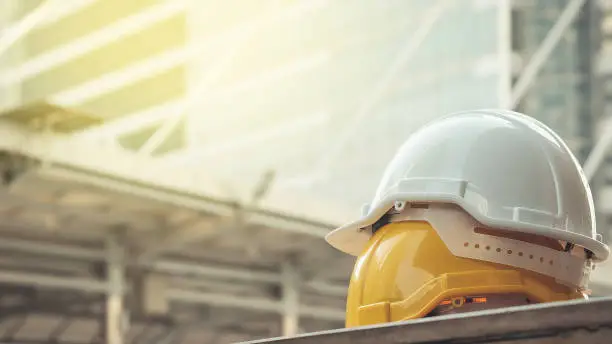 Photo of white, yellow hard safety helmet hat for safety project of workman as engineer or worker, on concrete floor on city