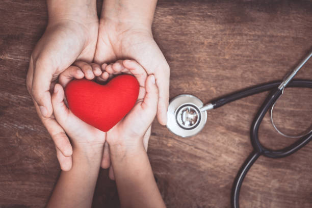 coeur rouge sur les mains de femme et enfant, avec stéthoscope du médecin sur fond en bois - stethoscope medicine doctor illness photos et images de collection