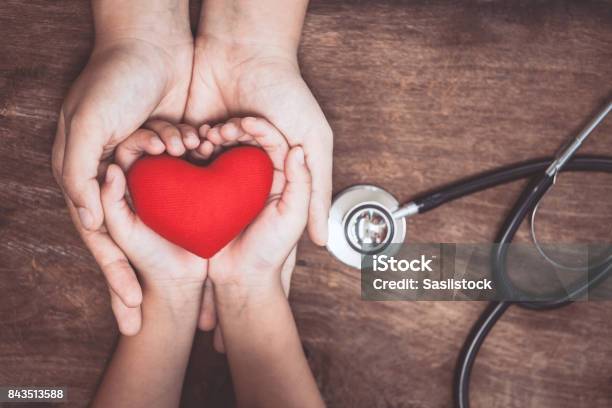 Red Heart On Woman And Child Hands And With Doctors Stethoscope On Wooden Background Stock Photo - Download Image Now