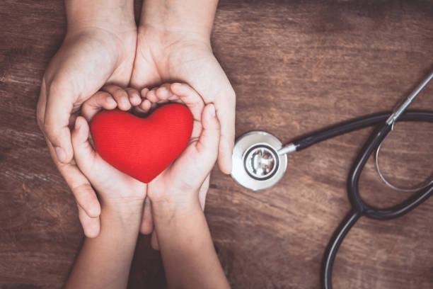 красное сердце на женских и детских руках и с стетоскопом врача на деревянном фоне - здоровье клуб стоковые фото и изображения