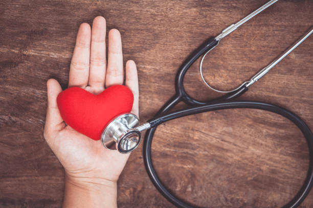 istock Red heart on woman's hand with doctor's stethoscope on wooden background 843513800
