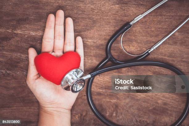 Red Heart On Womans Hand With Doctors Stethoscope On Wooden Background Stock Photo - Download Image Now