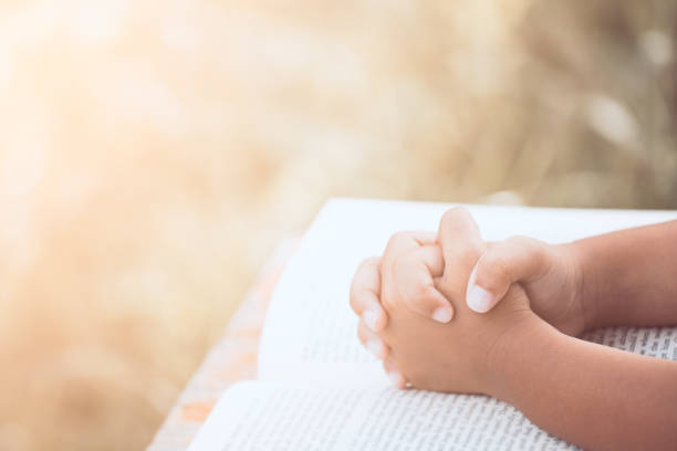 Little child girl hands folded in prayer on a Holy Bible stock photo