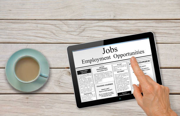 Online job hunting Hand with computer tablet reading employment ads on table with coffee stock photo