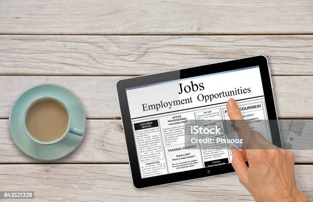 Online Job Hunting Hand With Computer Tablet Reading Employment Ads On Table With Coffee Stock Photo - Download Image Now