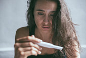 Woman holding pregnancy test with depressed worried face expression