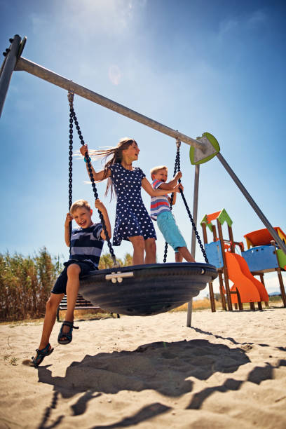 Children playing in the playground. Brothers and sister are having fun together on a big swing.