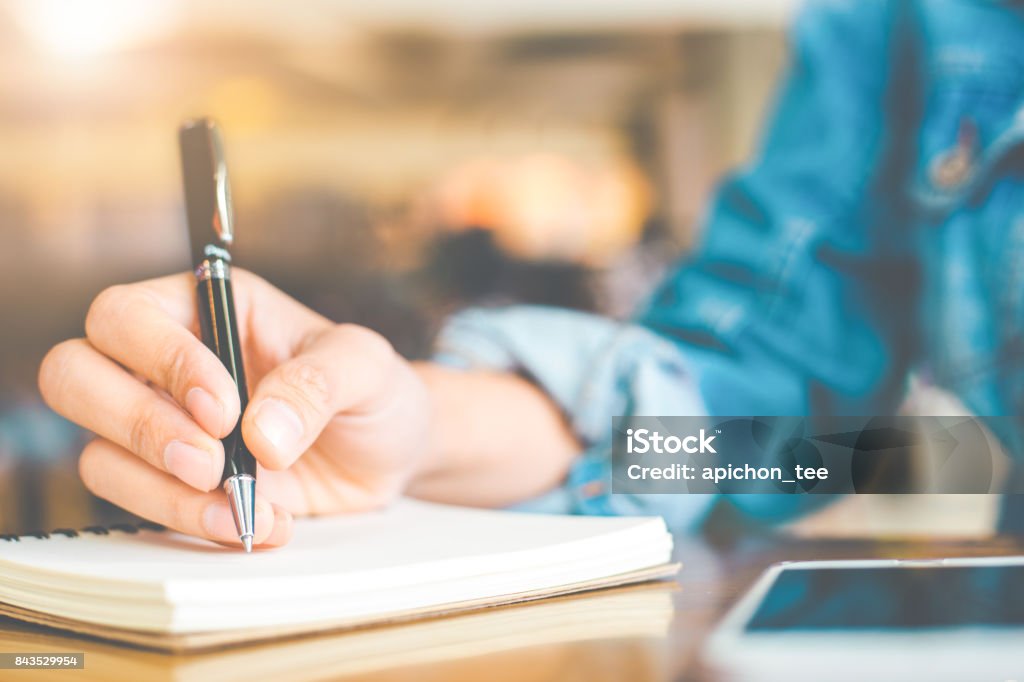 Zarte Frauenhand schreiben mit einem Stift auf einem hölzernen Schreibtisch auf einem Notizblock. - Lizenzfrei Buch Stock-Foto