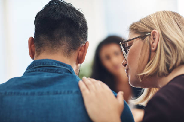 I know it hurts and I'm here for you Shot of a wife consoling her husband during a counseling session with a therapist hand on shoulder photos stock pictures, royalty-free photos & images