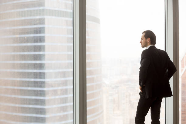 istock Serious young businessman standing in modern office, looking outside the window. 843545172