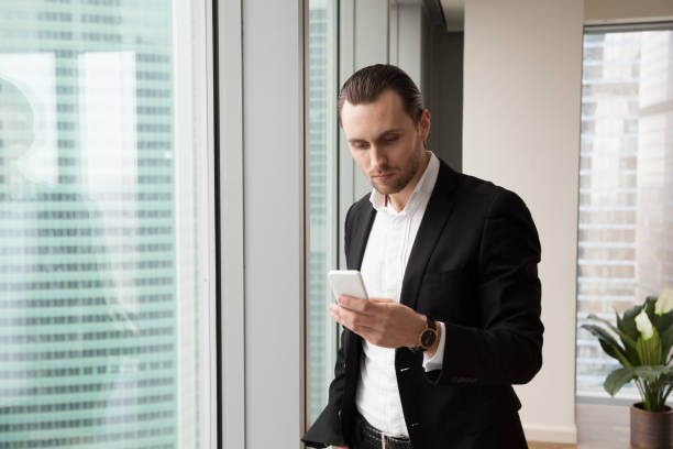 istock Serious young handsome businessman in modern office looking at cellphone 843545234