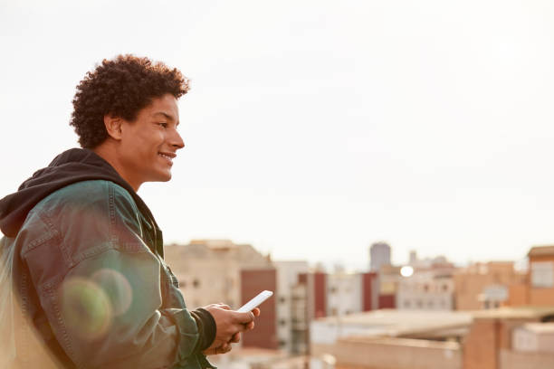 istock Smiling young man sitting with mobile phone at rooftop 843548460