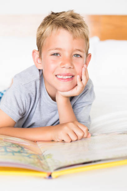istock Cheerful blonde boy lying on bed reading a storybook 843550306