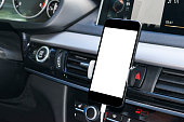 Smartphone in a car use for Navigate or GPS. Driving a car with Smartphone in holder. Mobile phone with isolatede white screen. Blank empty screen. copy space. Empty space for text. modern car interior details.