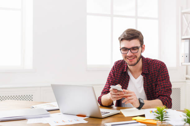 istock Young happy businessman in office using cell phone by the laptop 843561550