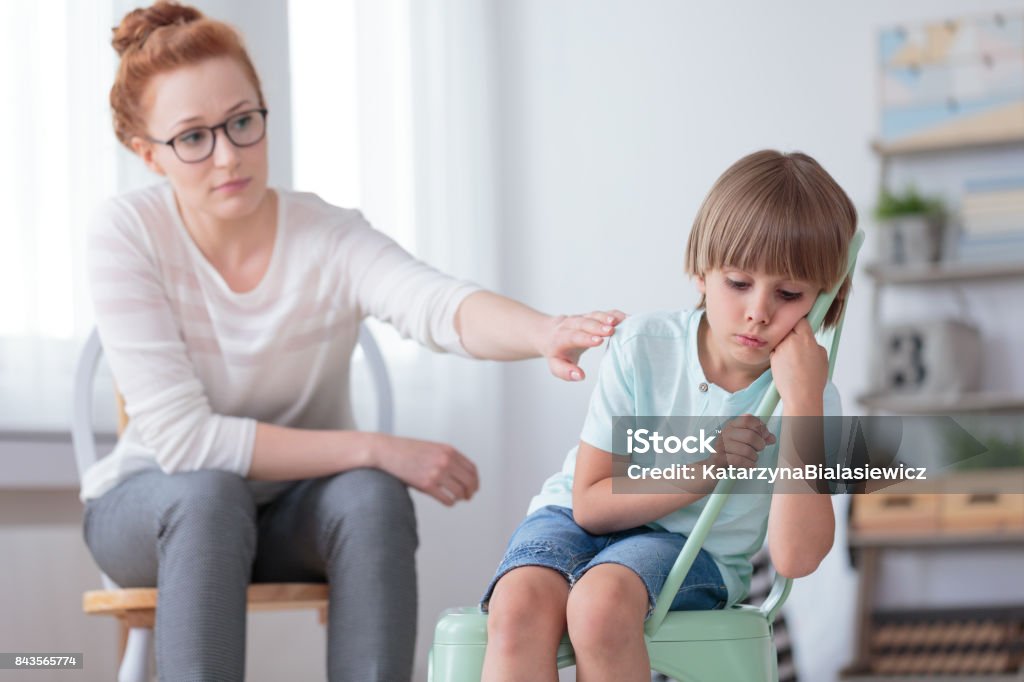 Sad autistic boy and psychotherapist Sad autistic boy sitting on mint chair during session with red haired psychotherapist Child Stock Photo