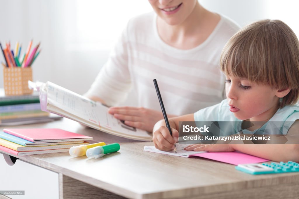 Boy focusing on homework Boy focusing on homework while sitting with mother at desk with notebook and colored pens Child Stock Photo