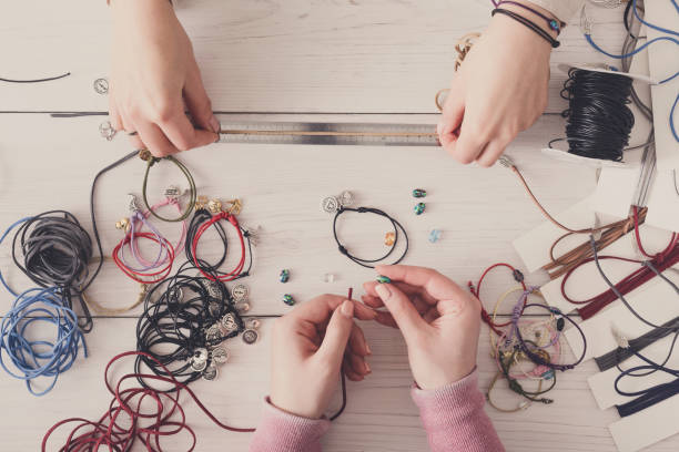 Handmade jewelry making, female hobby. Two women creating bracelets at home workshop, top view on workplace. Fashion, handicraft concept
