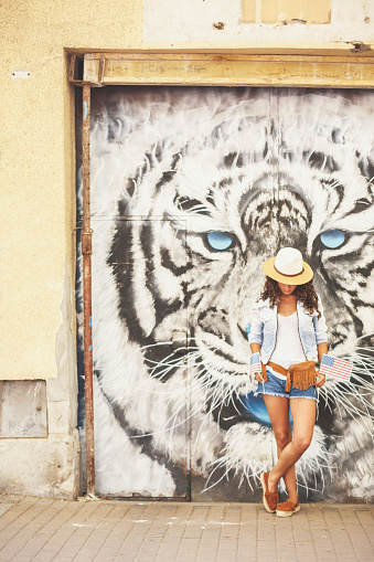 A girl in front of a mural with tiger head motif. She is looking down, holding two little american flags.