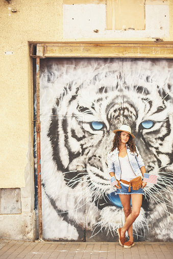 Beautiful american girl is standing in front of a tiger head mural, and holding little american flags.