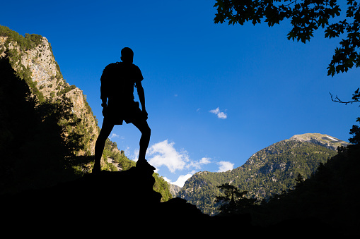 Looking at view at edge of the canyon. Success and achievement silhouette hiking or climbing, man with backpack celebrating beautiful inspirational landscape. Samaria Gorge canyon in Crete Greece.