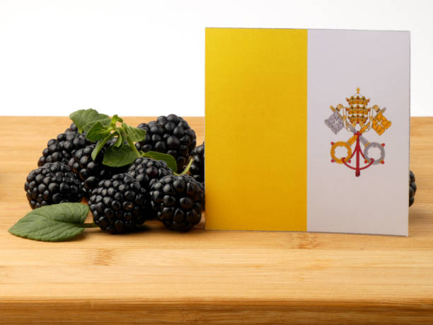 istock Vatican flag on a wooden panel with blackberries isolated on a white background 843595718