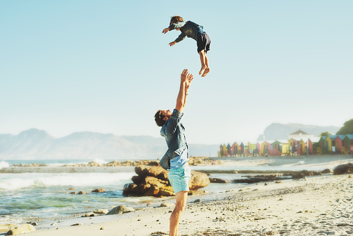 Shot of a young Father tossing his son into the air at the beach