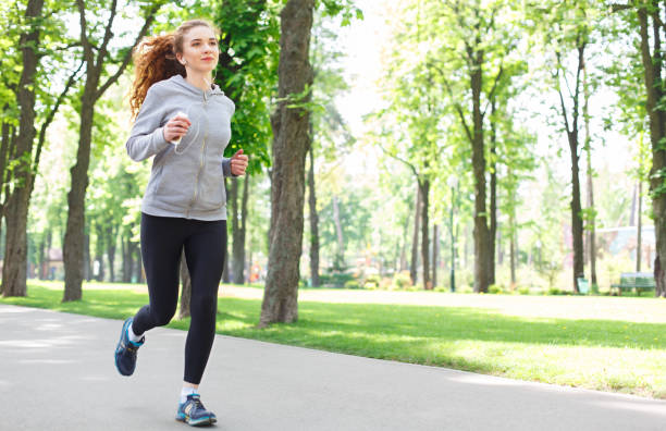 istock Young woman jogging in green park, copy space 843629360