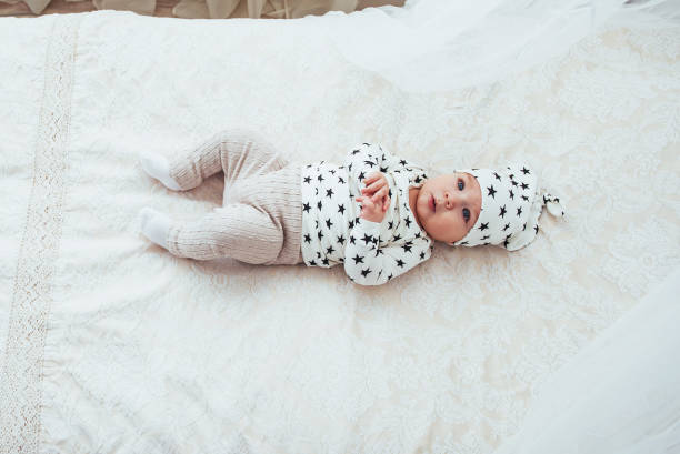 nouveau-né, vêtu d’un costume blanc et d’étoiles noires est un blanc moelleux lit dans le studio - newborn little girls baby lying down photos et images de collection