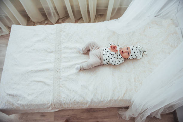 nouveau-né, vêtu d’un costume blanc et d’étoiles noires est un blanc moelleux lit dans le studio - newborn little girls baby lying down photos et images de collection