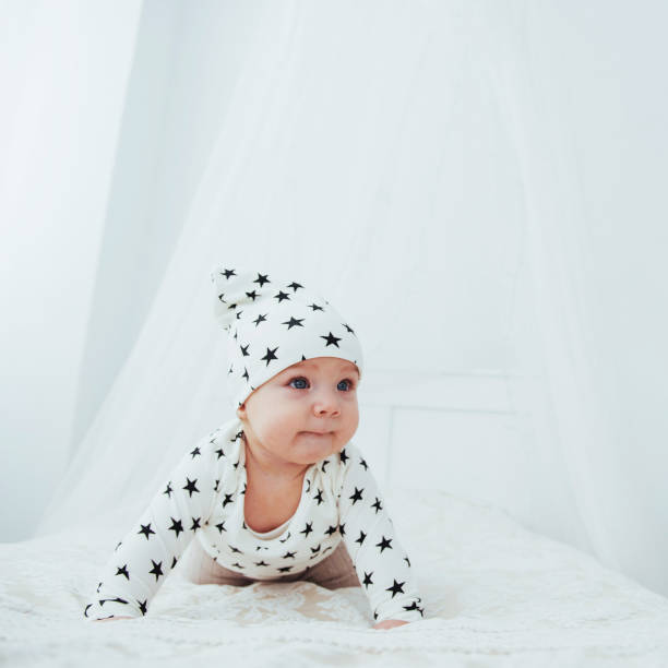 nouveau-né, vêtu d’un costume blanc et d’étoiles noires est un blanc moelleux lit dans le studio - newborn little girls baby lying down photos et images de collection