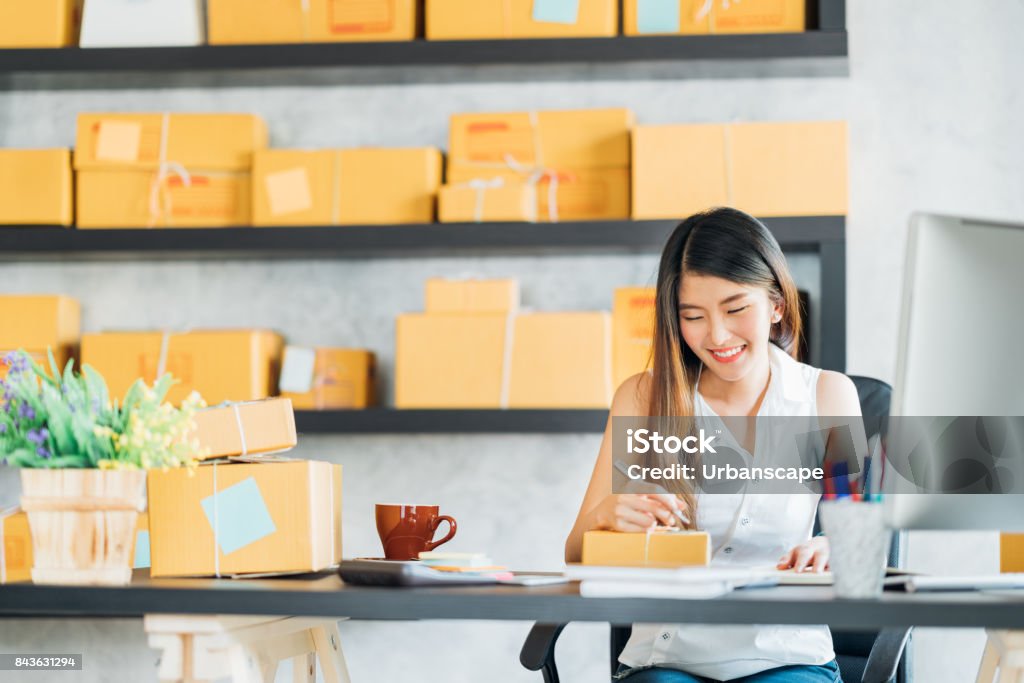 Young Asian small business owner working at home office, taking note on purchase orders. Online marketing packaging delivery, startup SME entrepreneur or freelance woman concept E-commerce Stock Photo