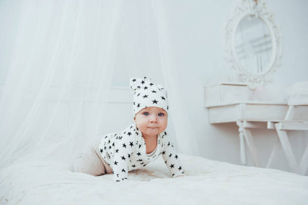 nouveau-né, vêtu d’un costume blanc et d’étoiles noires est un blanc moelleux lit dans le studio - newborn little girls baby lying down photos et images de collection