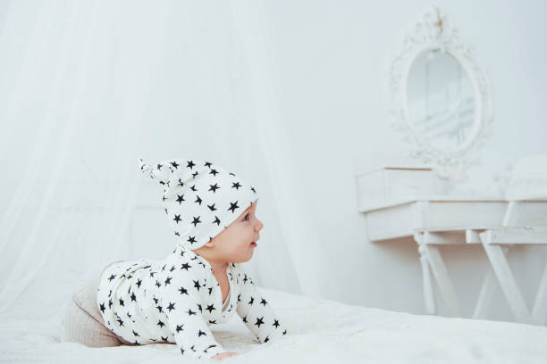 nouveau-né, vêtu d’un costume blanc et d’étoiles noires est un blanc moelleux lit dans le studio - newborn little girls baby lying down photos et images de collection