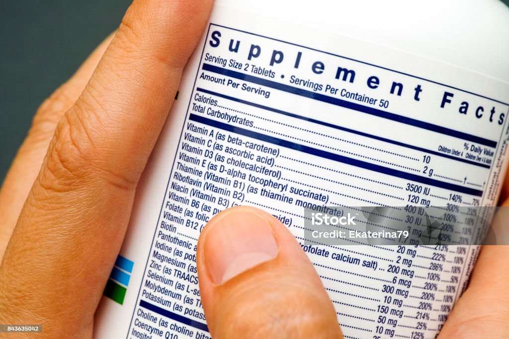 White plastic jar with supplement facts of multivitamins in woman hands. Nutritional Supplement Stock Photo