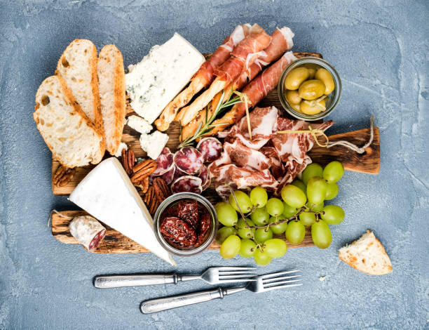 Cheese and meat appetizer selection or wine snack set. Variety of , salami, prosciutto, bread sticks, baguette, honey, grapes, olives, sun-dried tomatoes, pecan nuts over grey concrete textured backdrop, top vie Cheese and meat appetizer selection. Prosciutto di Parma, salami, bread sticks, baguette slices, olives, sun-dried tomatoes, grapes and nuts on rustic wooden board over grey concrete textured backdrop, top view prosciutto brie stock pictures, royalty-free photos & images