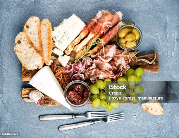 Cheese And Meat Appetizer Selection Or Wine Snack Set Variety Of Salami Prosciutto Bread Sticks Baguette Honey Grapes Olives Sundried Tomatoes Pecan Nuts Over Grey Concrete Textured Backdrop Top Vie Stock Photo - Download Image Now