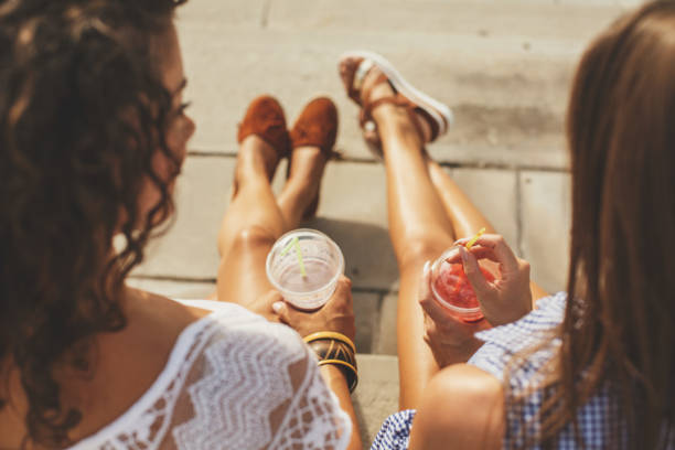Relaxing and tanning Two female friends are sitting on the staircase, drinking juice and enjoying the sun. non alcoholic beverage stock pictures, royalty-free photos & images